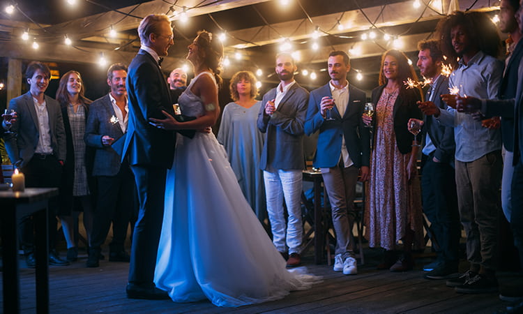 A bride and groom smile at each other while guests cheer